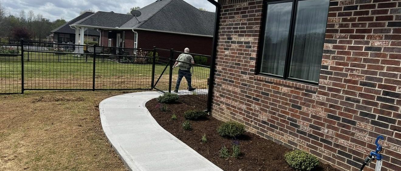 Concrete walkway and landscaped beds along a black metal fence in Union City, TN